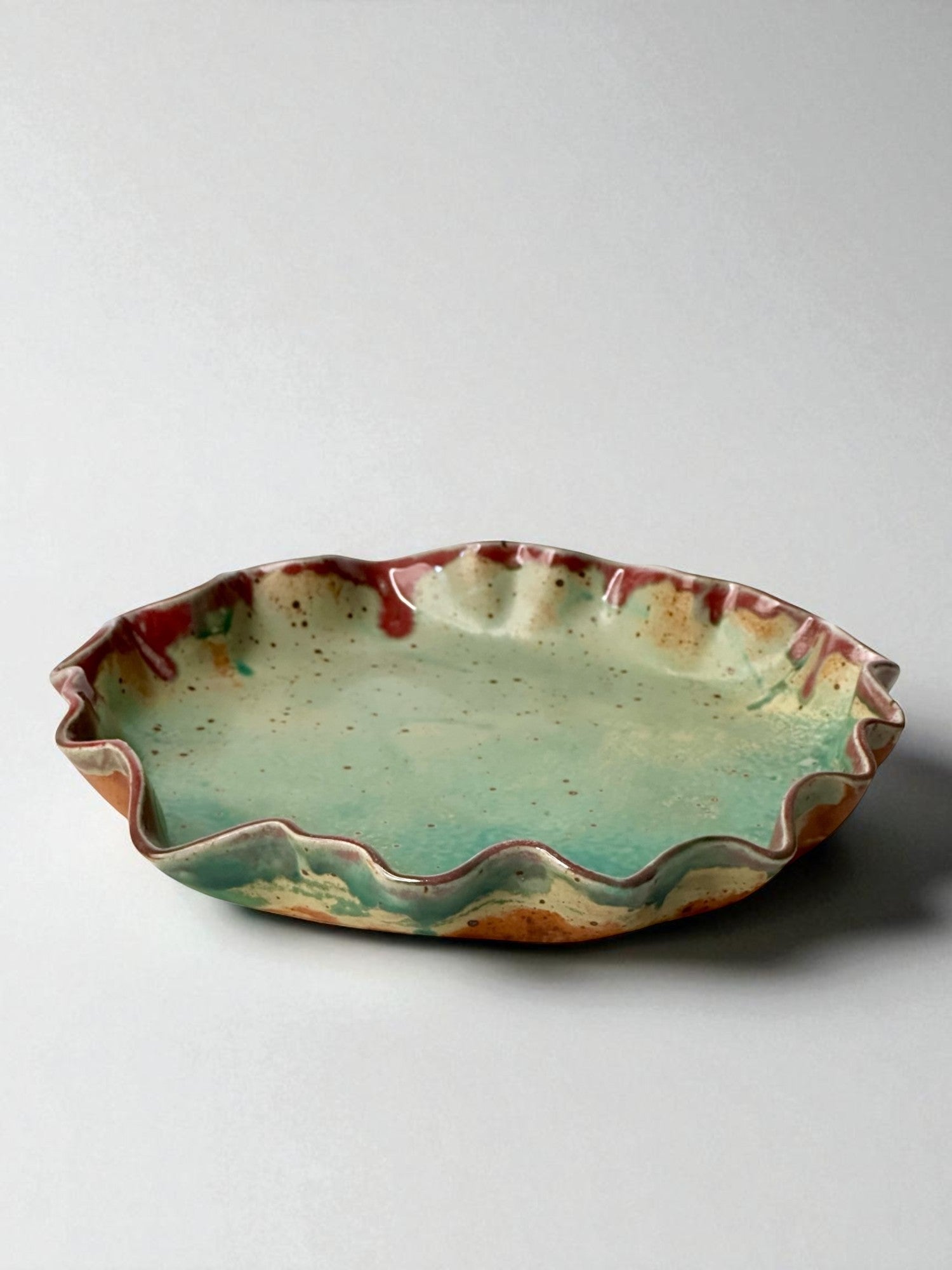 Green and red ceramic pie plate with wavy edge on a white background