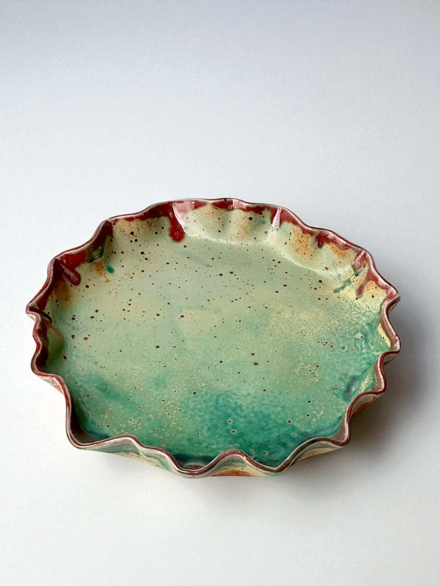 Green and red ceramic pie plate with a wavy edge seen from above on a white background