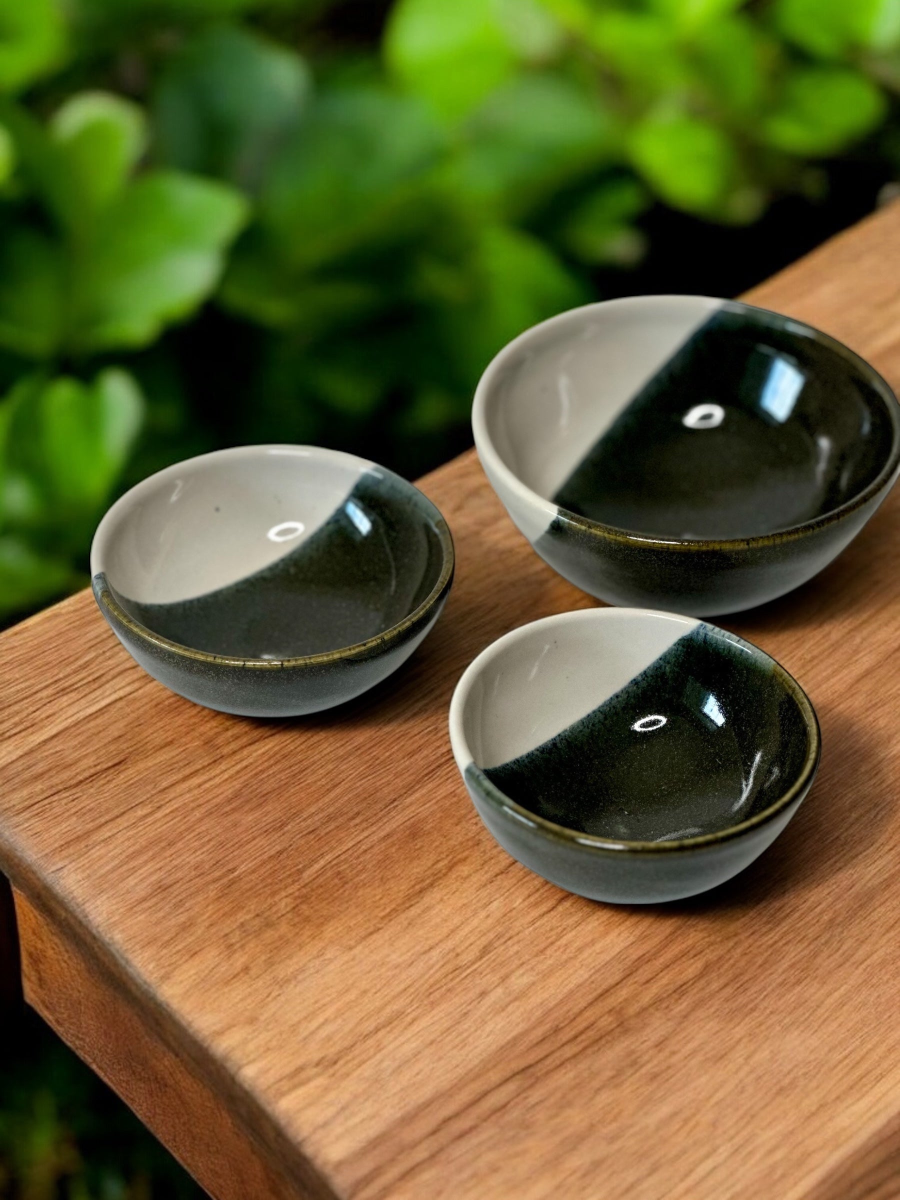 Three ceramic bowls with half black and half white on a wooden surface with greenery in the background